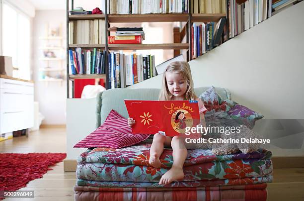 a 3 years old girl reading a book on a sofa - 2 3 years stock pictures, royalty-free photos & images