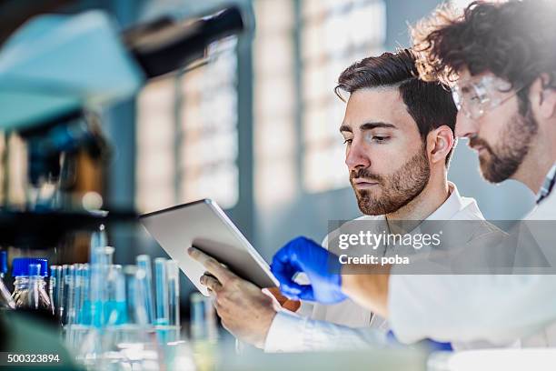 two scientist using digital tablet in laboratory - natuurkunde stockfoto's en -beelden