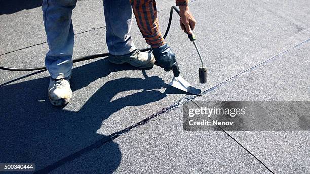 roofer preparing part of bitumen roofing felt roll for melting by gas heater torch flame - membrane stock pictures, royalty-free photos & images