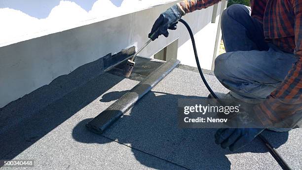 roofer preparing part of bitumen roofing felt roll for melting by gas heater torch flame - plat dak stockfoto's en -beelden