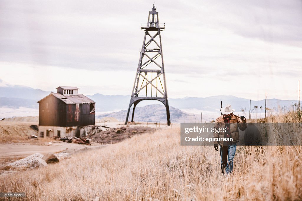 Man carrying pickaxe walking by old oil drill and barn