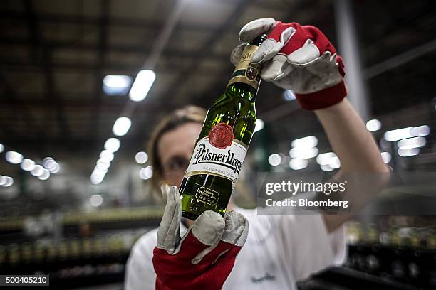 Worker holds up a bottle of beer against the light during a quality control inspection on the production line at the Pilsner Urquell brewery,...