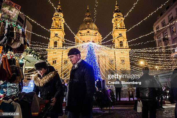 Shoppers browse alpaca wool products at a Christmas market as an illuminated Christmas tree stands in front of St. Stephen's Basilica in Budapest,...