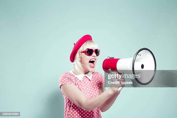 cute blonde young woman shouting into megaphone - roze jurk stockfoto's en -beelden