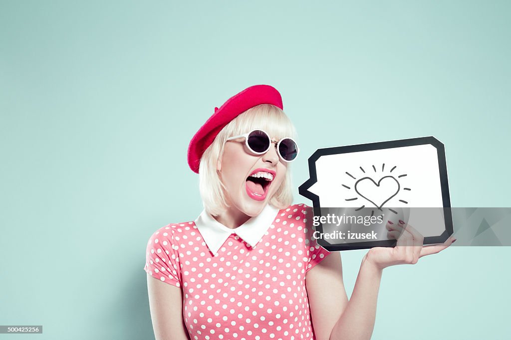 Excited blonde young woman holding speech bubble with drawn heart