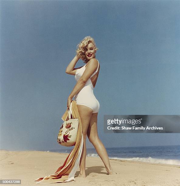 Marilyn Monroe on the beach looking back at the camera with a towel and beach bag in her hand in 1957 in Amagansett, New York.
