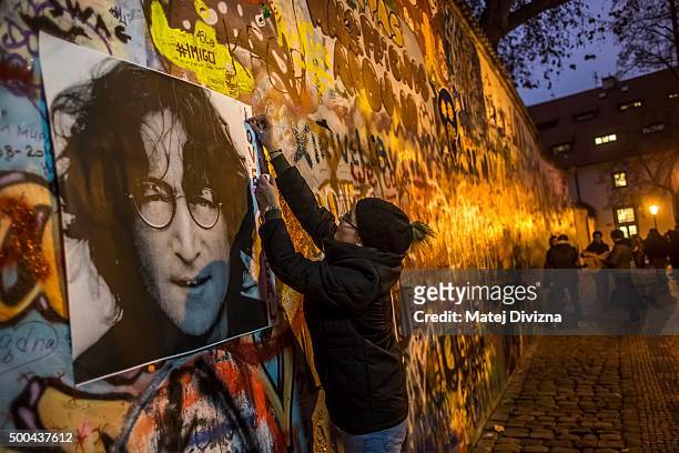 Woman attaches the placard with picture of John Lennon on the Lennon Wall, the memorial dedicated to the late John Lennon on the 35th anniversary of...