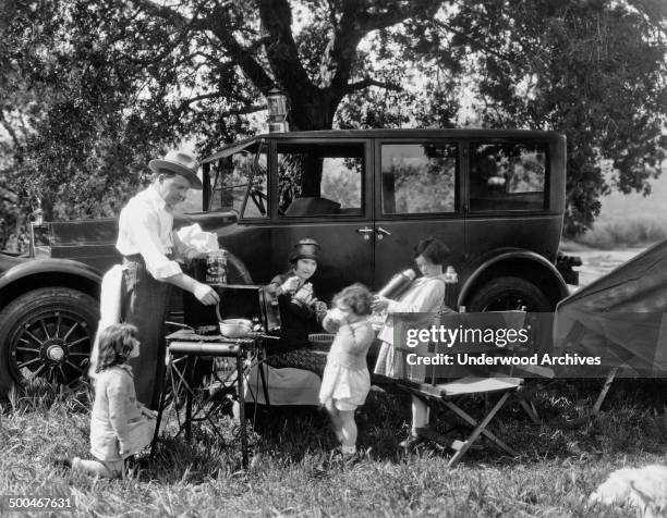 Family cooking a meal while camping with their Pierce Arrow automobile, circa 1928.