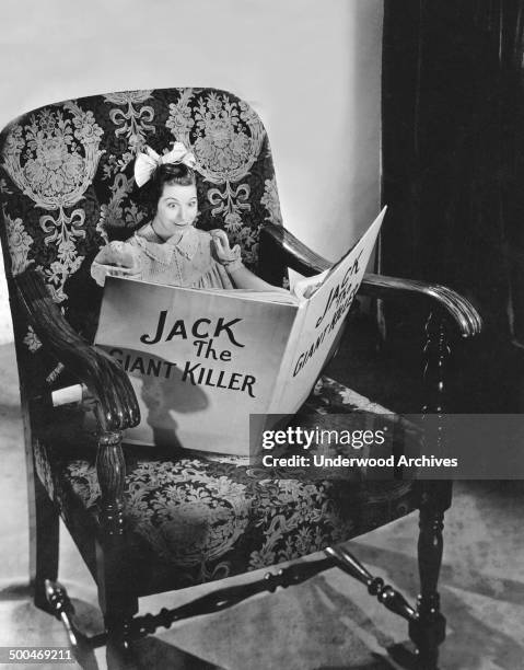 Actress Fanny Brice reading a book in an oversized chair in her role as Baby Snooks on the 'Good News' Radio program, Hollywood, California, 1938.