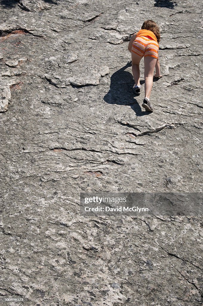 Young girl climbing up rock surface