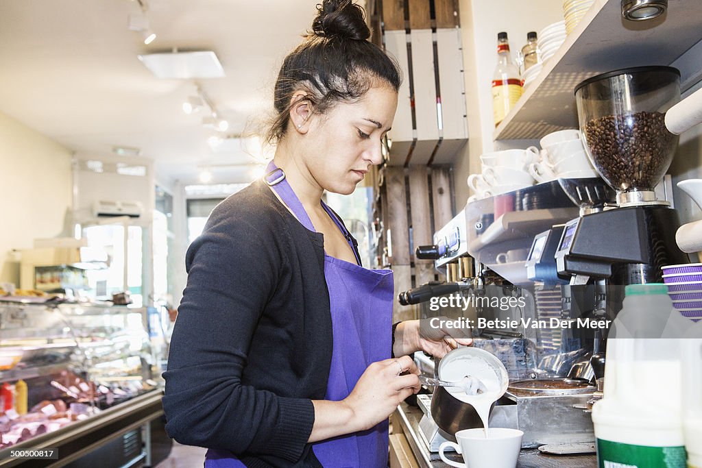 Female waitress making coffee in delicatessen shop