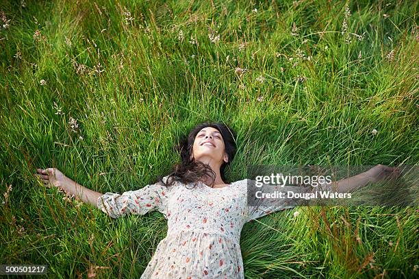 woman laying in meadow with arms stretched - im gras liegen stock-fotos und bilder