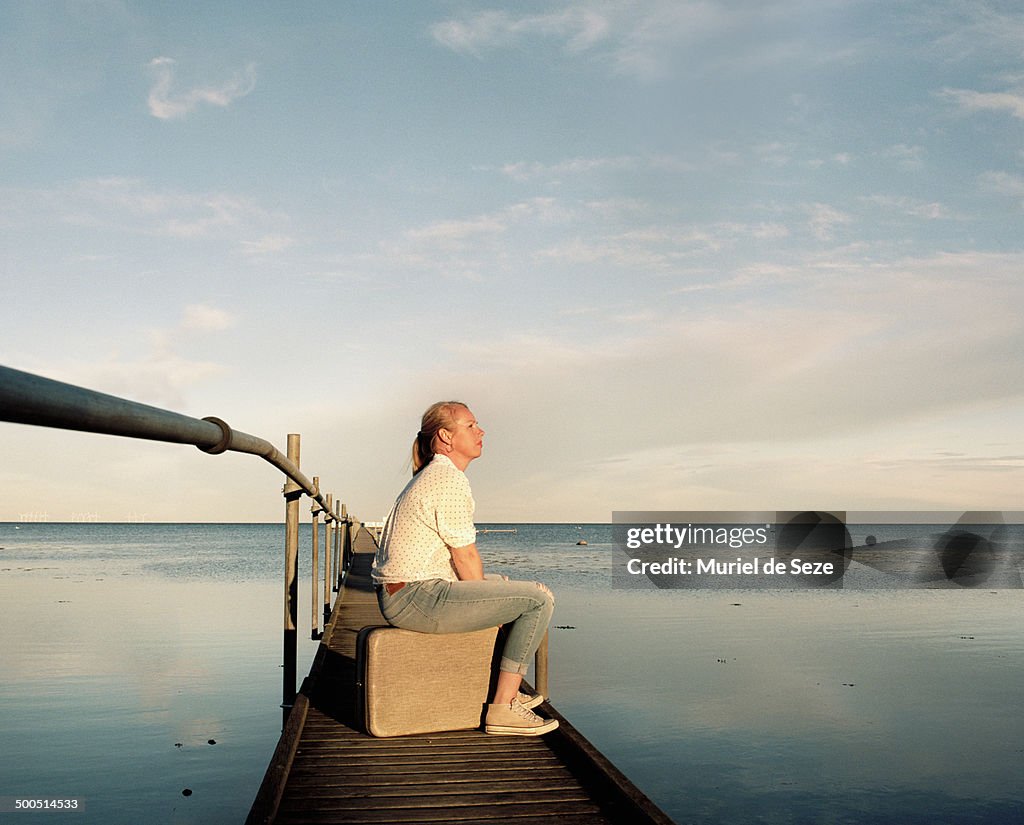 Woman sitting on suitcase by sea