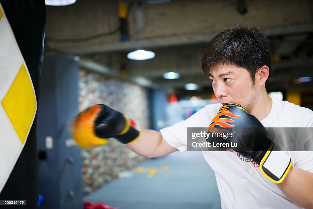 Male boxer training and hitting punch bag in gym.