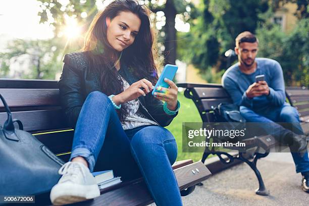 pareja joven en el parque sms en smartphones - conquista fotografías e imágenes de stock