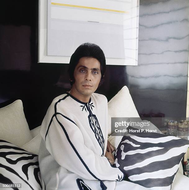 Fashion designer Valentino wearing a white tunic edged in black embroidery of his design, surrounded by plain white and zebra-stripe pillows in the...