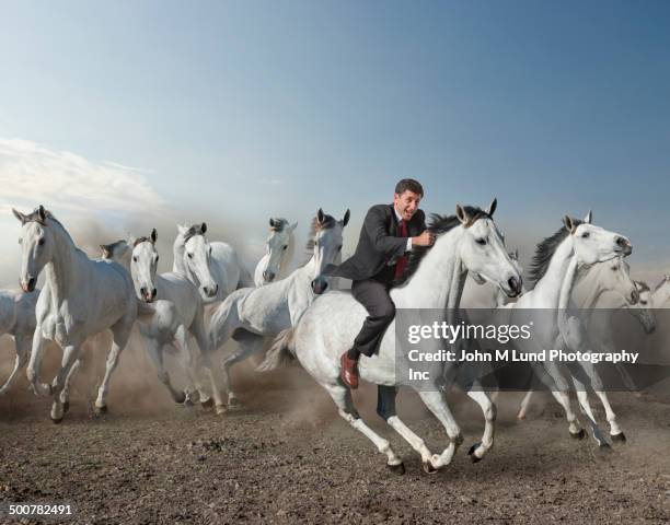 caucasian businessman riding wild horse in desert - andare a cavallo foto e immagini stock