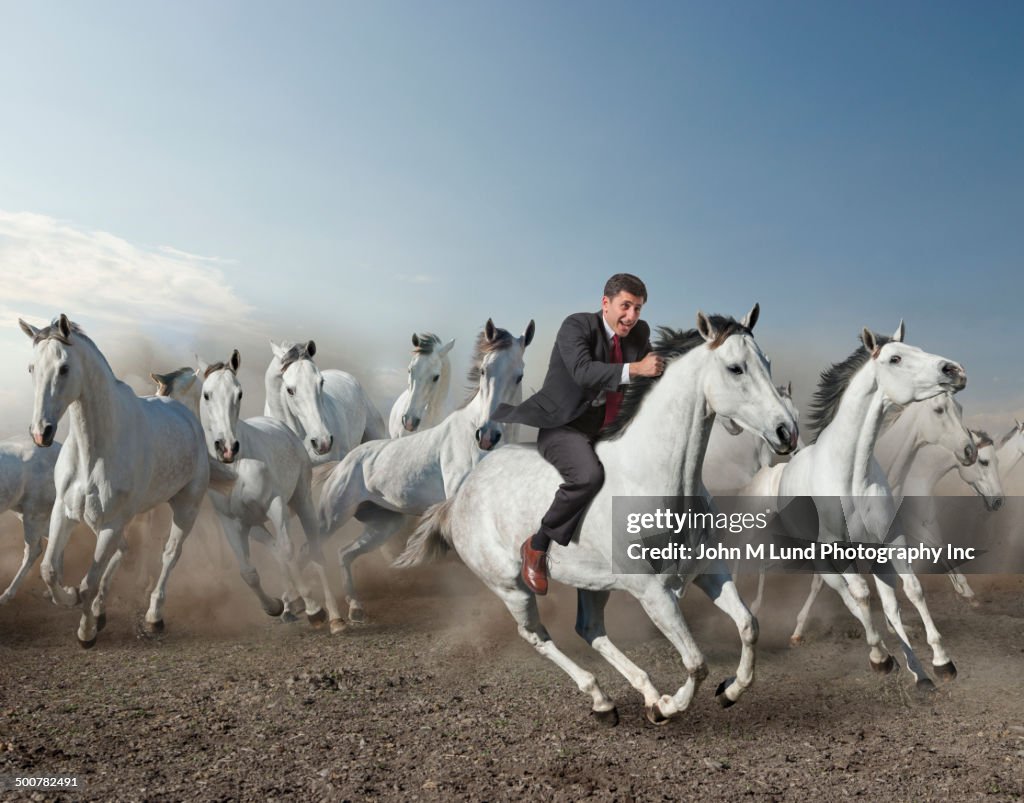 Caucasian businessman riding wild horse in desert