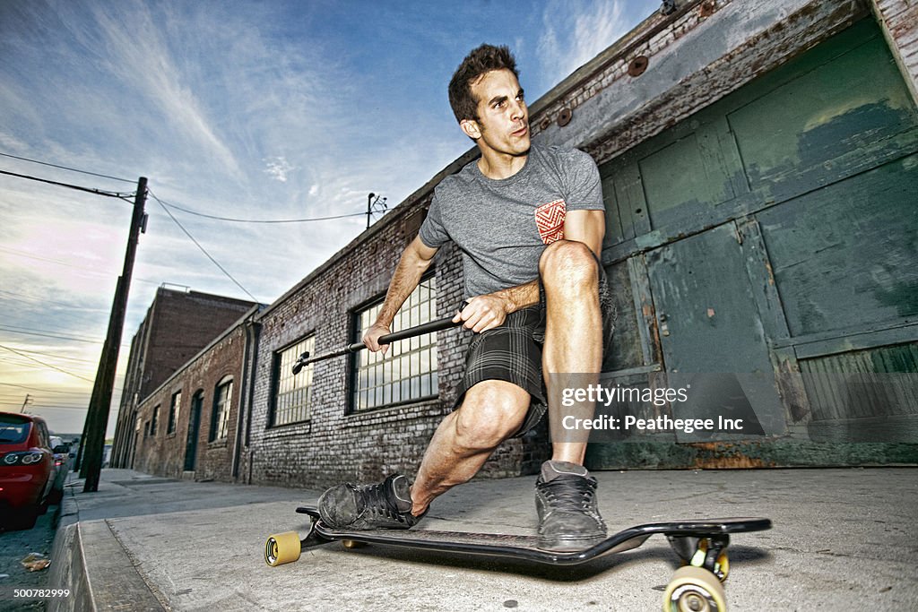 Caucasian man riding skateboard with land paddle