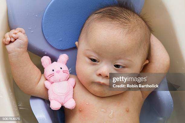 mixed race down syndrome baby laying in plastic bathtub - baby bath toys stock pictures, royalty-free photos & images