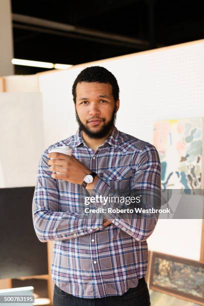 mixed race artist drinking coffee in studio - mixed race man standing studio stockfoto's en -beelden