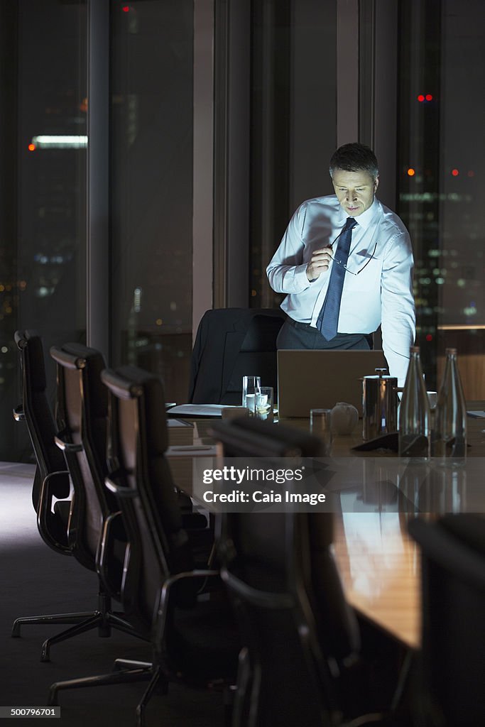 Businessman working at laptop in conference room at night