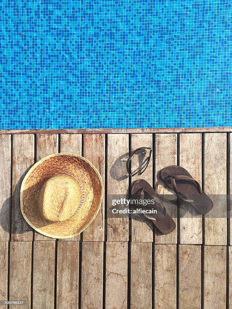 Sun hat, flip-flops and sunglasses by swimming pool