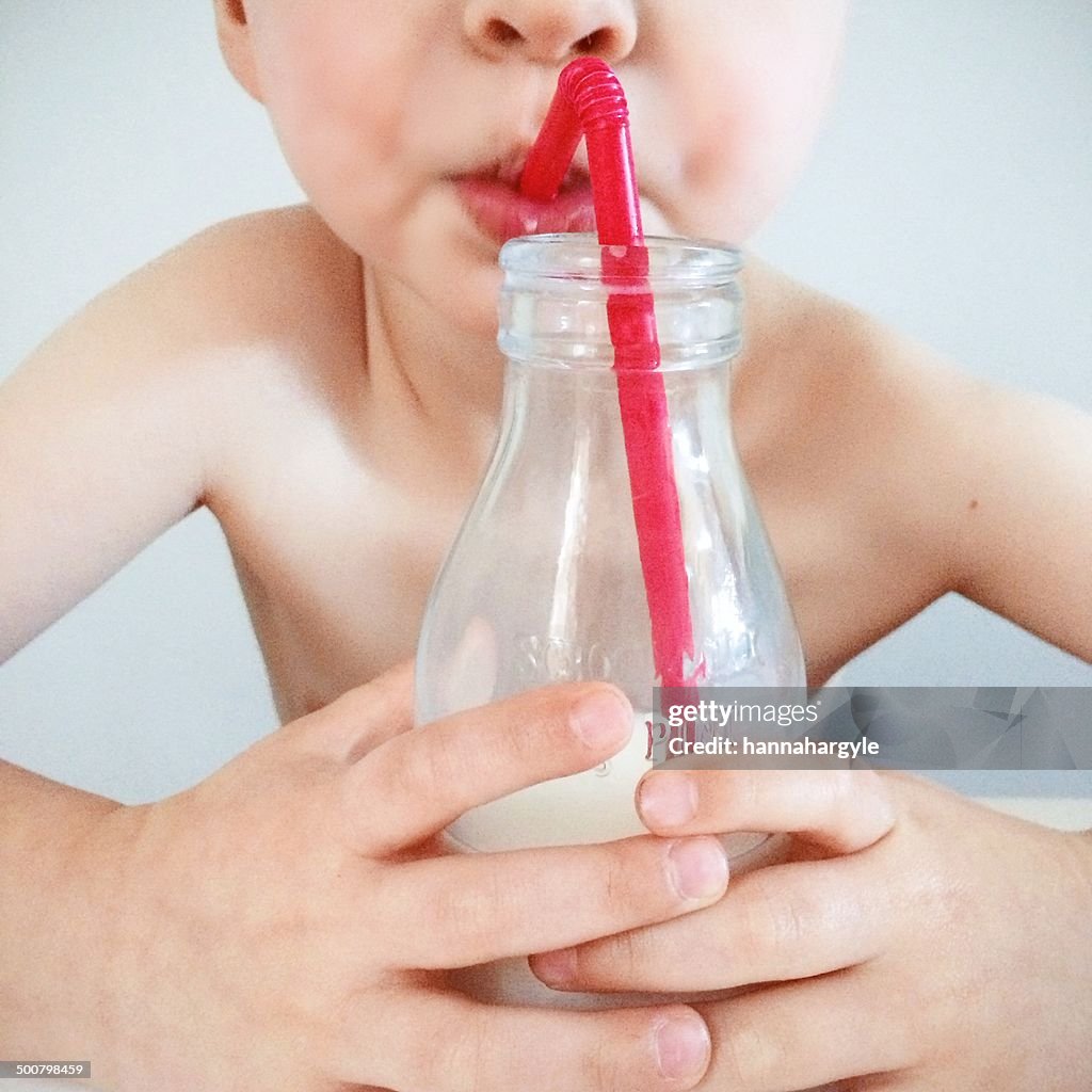 Boy drinking from milk bottle with a straw