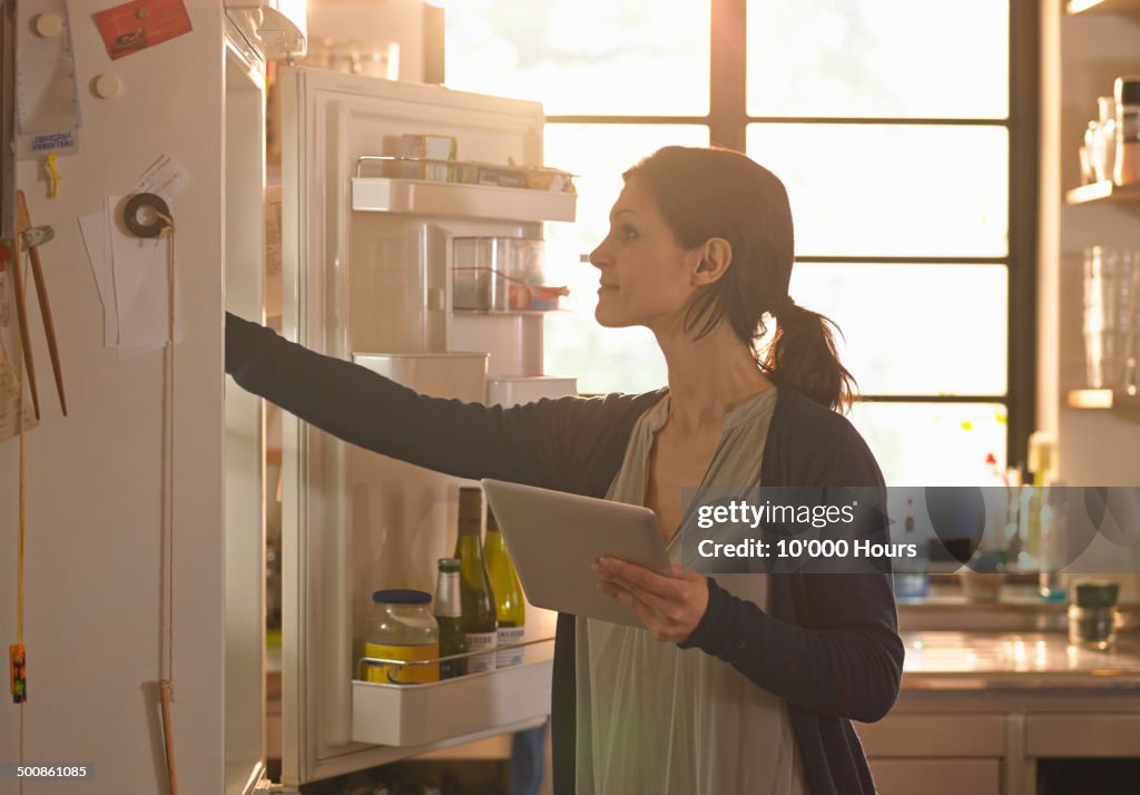 Woman holding an tablet computer whilst looking in the fridge