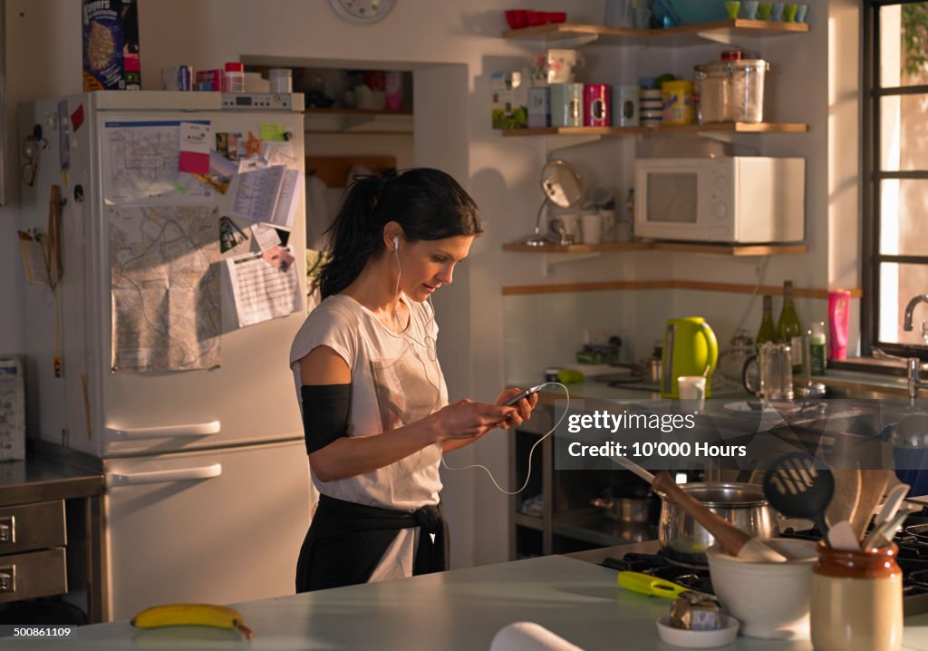 Woman in kitchen preparing music for a run