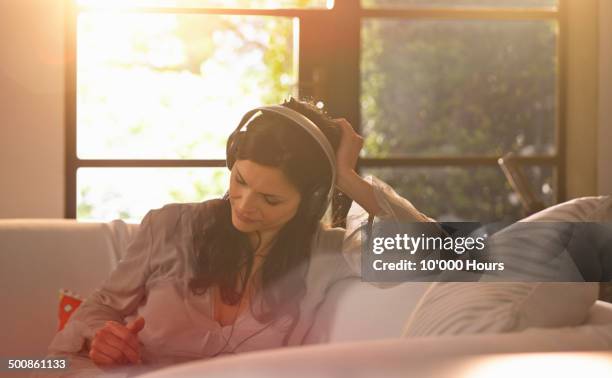 a woman relaxing at home wearing headphones - protuberanz stock-fotos und bilder