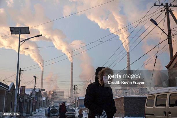 Smoke billows from stacks as a Chinese woman wears as mask while walking in a neighborhood next to a coal fired power plant on November 26, 2015 in...