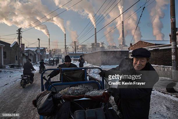 Smoke billows from stacks as Chinese men pull a tricycle in a neighborhood next to a coal fired power plant on November 26, 2015 in Shanxi, China. A...