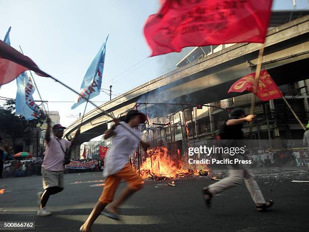 Filipino protesters holding organizational flags run around the burning remains of an effrigy of Philippine President Benigno Aquino during a protest...