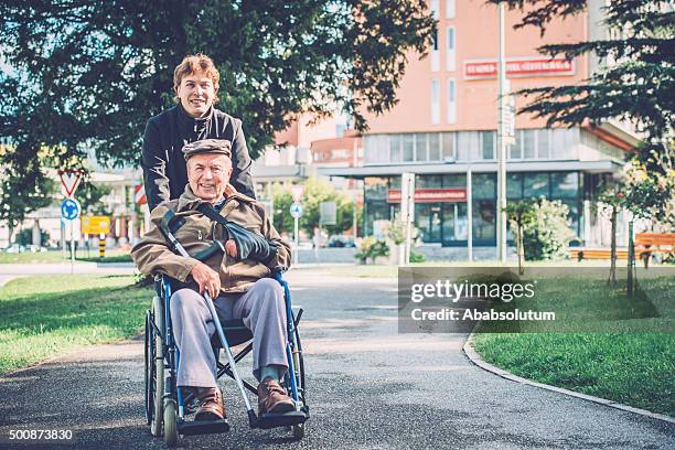 happy senior hombre en silla de ruedas y nieto en la ciudad - geriatria fotografías e imágenes de stock