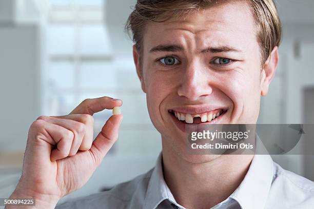 young man holding his missing tooth, smiling - hueco entre dientes fotografías e imágenes de stock