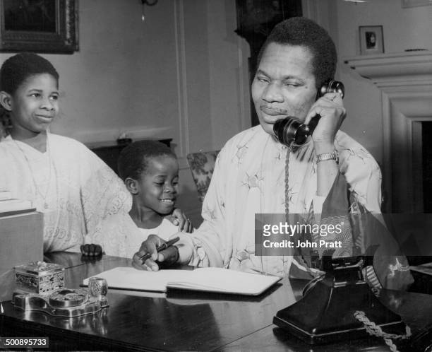 Michael Okorodudu, West Nigerian representative in London, on the telephone at his desk, with his children Michael Jr and Ladi, circa 1955.