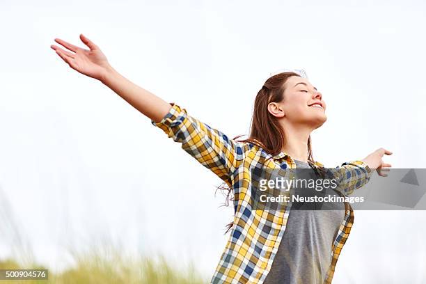 happy young woman with arms open against clear sky - zuiverheid stockfoto's en -beelden