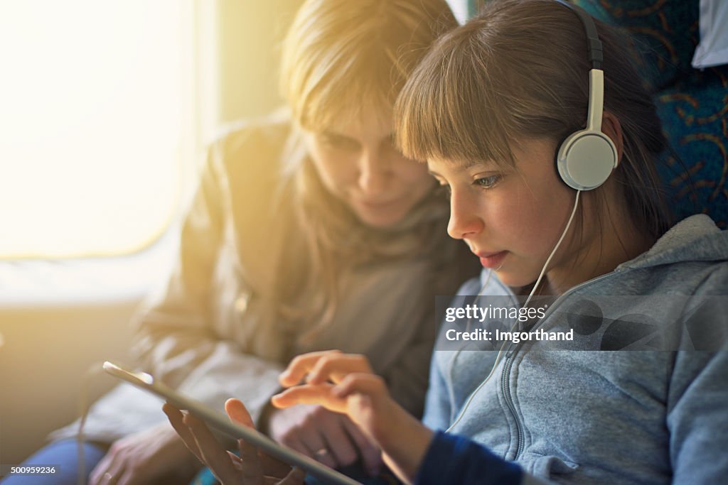 Girl with mother travelling on train and playing on tablet