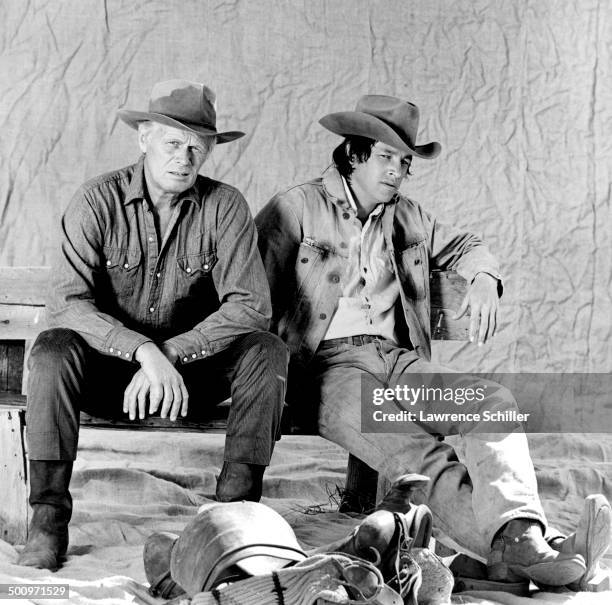 Portrait of American actors Richard Widmark and Frederic Forrest, both in costume, as they sit on a bench during the production of their film 'When...