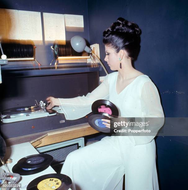 Young female disc jockey or DJ changes a selection of records on twin turntables in a night club in 1967.