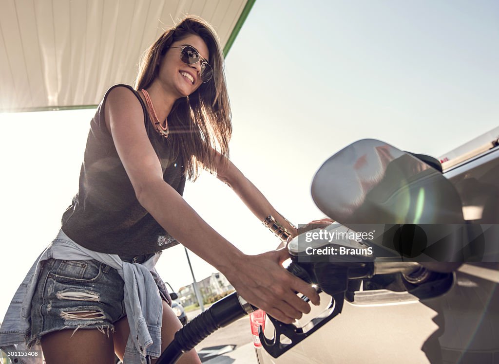 Mujer feliz echar combustible el tanque de la gasolina en bomba de combustible.