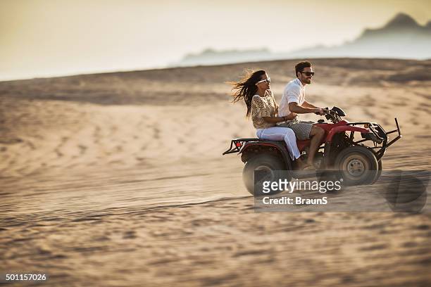 young happy couple having fun while driving on quad bike. - jeep desert stock pictures, royalty-free photos & images