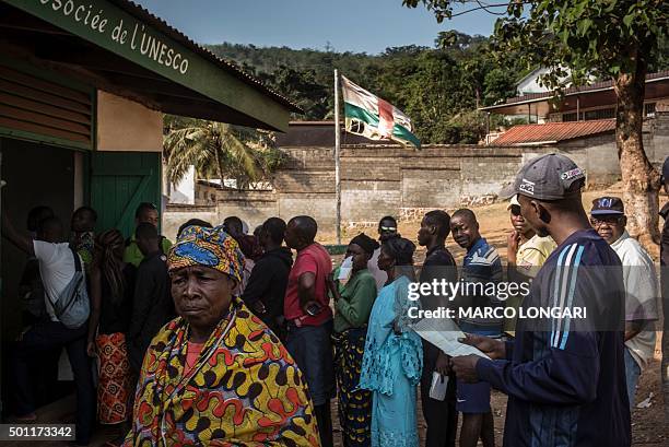 Battered Central African Republic flag flutters as voters queue outside a polling station in Bangui on December 13, 2015 to vote for the...