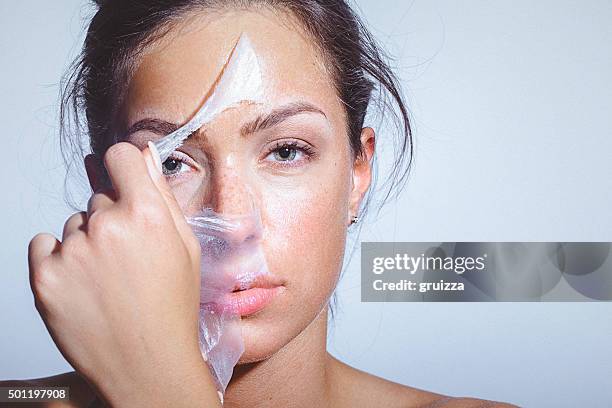 beauty portrait of a young woman applying-removing face mask - clay mask face woman stock pictures, royalty-free photos & images