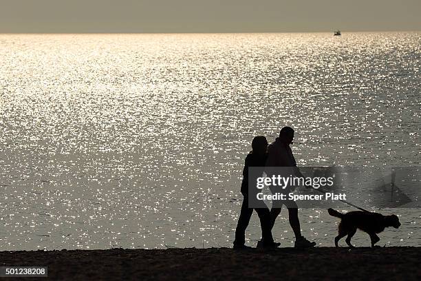 Couple walks a dog along a beach on December 13, 2015 in Fairfield, Connecticut. Temperatures across much of the New York metropolitan area continued...