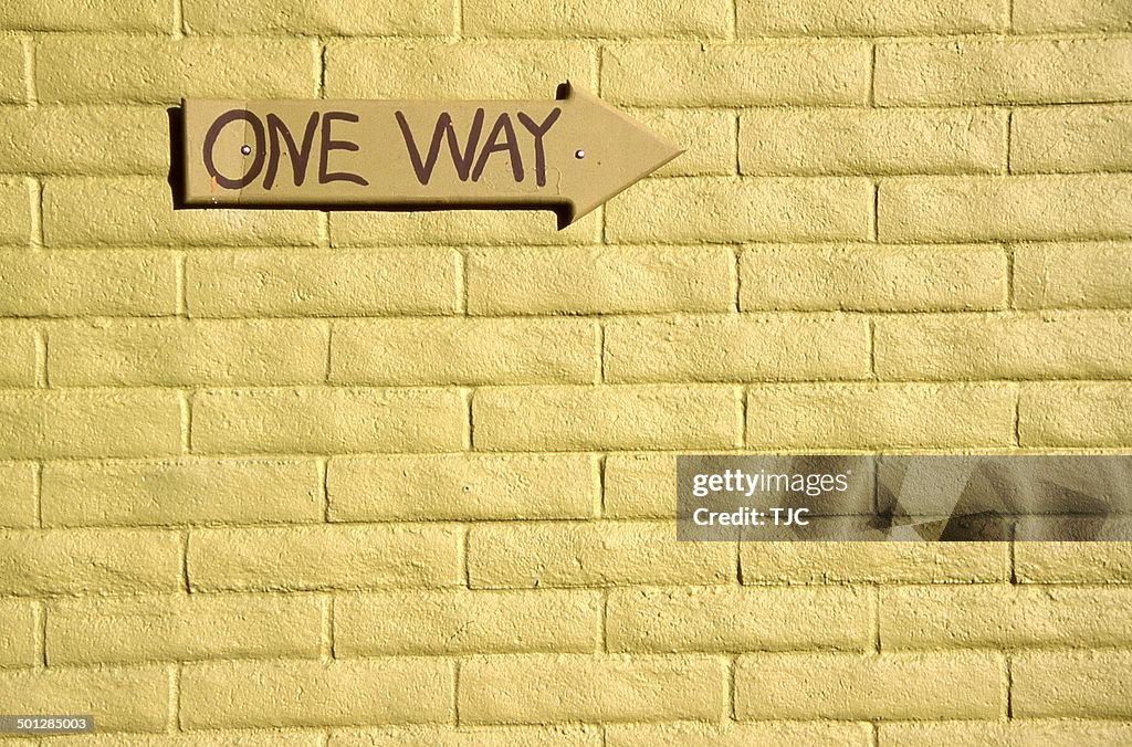 One-way sign on a yellow walll