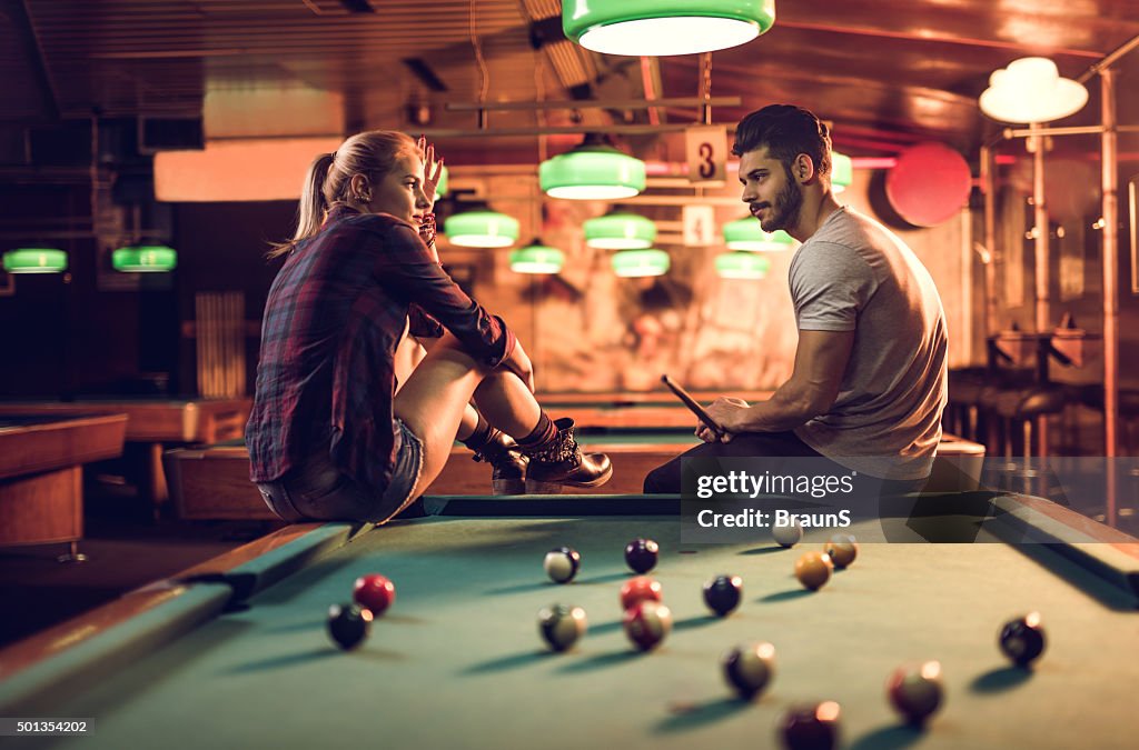 Couple sitting on a pool table in pub and talking.