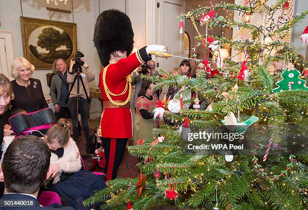 Captain Matt Wright of the Welsh Guards hangs a Christmas Decoration with his sword as Camilla, Duchess of Cornwall, patron of the Helen & Douglas...