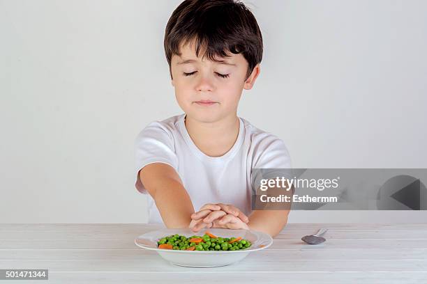 unhappy caucasian boy eating vegetables - picky eater stockfoto's en -beelden